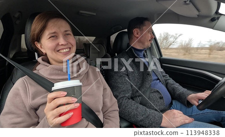 Smiling couple riding car talking drinking coffee together closeup. Happy man and woman pair family driving automobile enjoy countryside road trip friendly communication love and positive emotion 113948338
