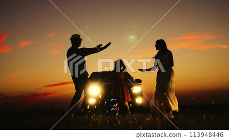Active family dancing near car in field at sunset silhouettes. Mom father kid child dancing hands against of car headlights sunset orange sky. Happy funny time with family in nature on travel trip. Active family dancing near car in field at sunset silhouettes. Mom father kid child dancing hands against of car headlights sunset orange sky. Happy funny time with family in nature on travel trip. 113948446