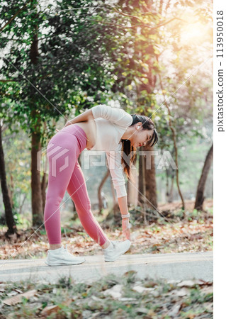 Active young woman taking a break to stretch her legs in a sunlit forested park. Active young woman taking a break to stretch her legs in a sunlit forested park. 113950018