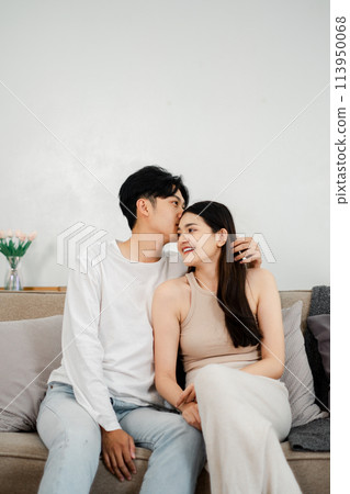 Couple shares a tender look filled with affection while seated comfortably on their couch, enhancing the feeling of a romantic home setting. Couple shares a tender look filled with affection while seated comfortably on their couch, enhancing the feeling of a romantic home setting. 113950068