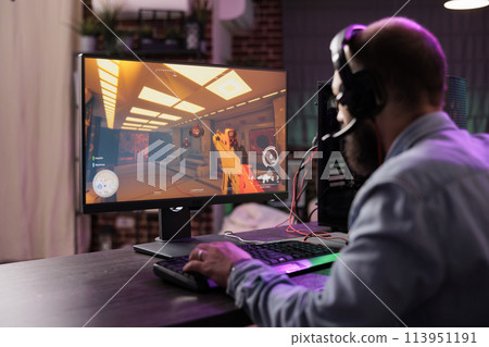 Gamer using professional grade level gaming system to avoid disruptive lag while playing esports tourneys. Man relaxing in brick wall apartment playing action shooting videogame late at night Gamer using professional grade level gaming system to avoid disruptive lag while playing esports tourneys. Man relaxing in brick wall apartment playing action shooting videogame late at night 113951191