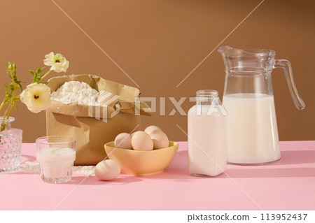 Brown background against cooking concept with milk, eggs and different ingredients decorated by a vase of flower on pink table. Blank space for text or presenting product 113952437
