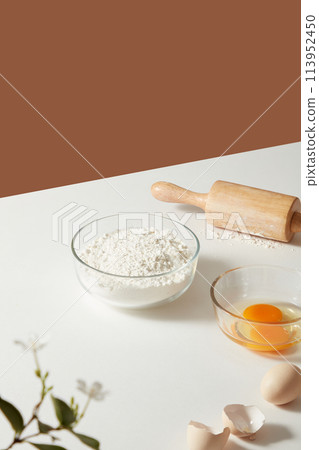 A glass of lemon juice and some pieces of sandwich on wooden dish. Decorated by notebook, a haft of lemon and flower vase on minimalism background. Advertising for organic products 113952450