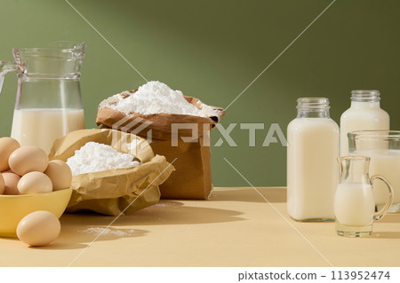 A set of glass bottle with fresh milk inside on the left, some baking ingredients lay on the right against forest green background. Photo has blank space or displaying product 113952474