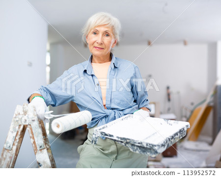 Mature woman painting walls with paint roller in refurbished room Mature woman painting walls with paint roller in refurbished room 113952572