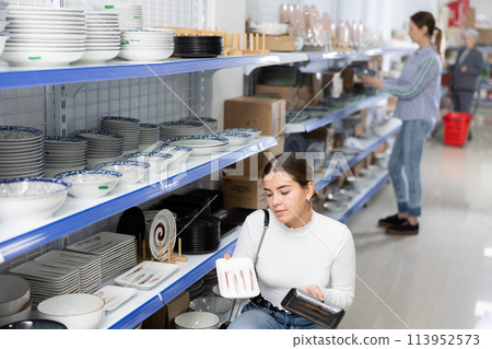 Young woman in supermarket is choosing square plates 113952573