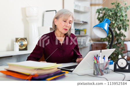 Busy focused aged female entrepreneur working with papers and laptop Busy focused aged female entrepreneur working with papers and laptop 113952584