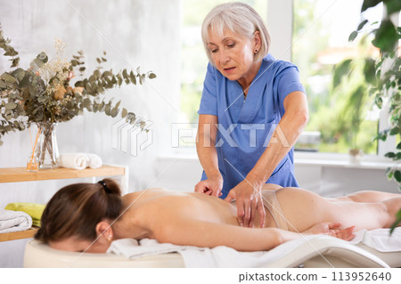 Skilled aged masseuse doing back pain relief massage to young woman Skilled aged masseuse doing back pain relief massage to young woman 113952640