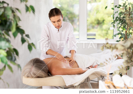 Unrecognizable elderly woman lies face down on couch and enjoy spa treatments, shoulder massage 113952661