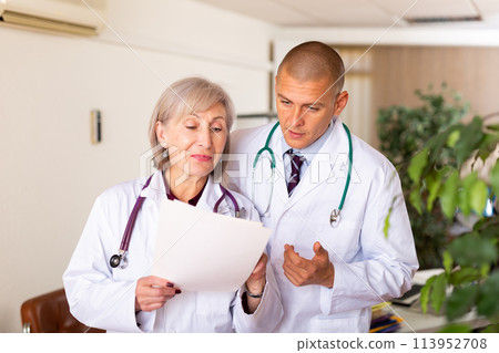 Two professional doctors discussing medical card of patient Two professional doctors discussing medical card of patient 113952708