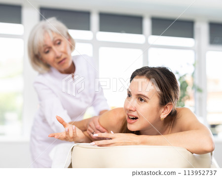 Young woman suffering from pain and discomfort during back massage session Young woman suffering from pain and discomfort during back massage session 113952737