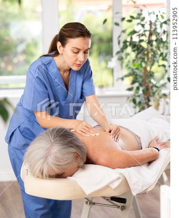 Unrecognizable elderly woman lies face down on couch and enjoy spa treatments, shoulder massage Unrecognizable elderly woman lies face down on couch and enjoy spa treatments, shoulder massage 113952905