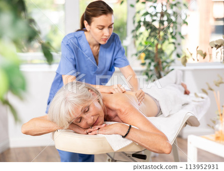 Aged woman relaxing in spa center during professional back massage Aged woman relaxing in spa center during professional back massage 113952931