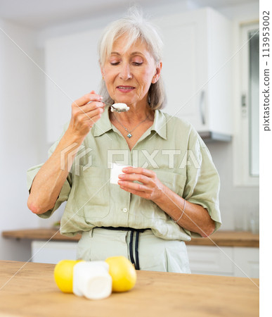Mature woman eating tasty yogurt in kitchen 113953002