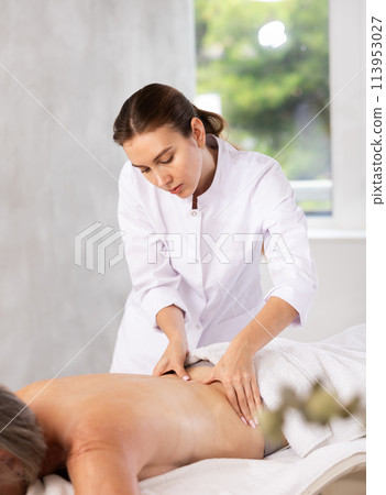 Skilled young masseuse doing back pain relief massage to elderly woman Skilled young masseuse doing back pain relief massage to elderly woman 113953027