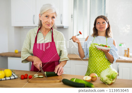 Senior woman and her adult daughter cooking salad together Senior woman and her adult daughter cooking salad together 113953045