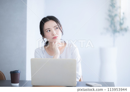 Cute young Japanese (Asian) woman with hand on chin thinking while using a computer Negative image 113953944