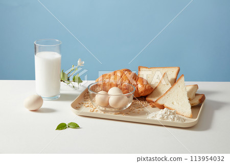 Front view photo of cooking or baking concept with croissant, sandwich, eggs and fresh milk on blue background. Empty pace for designing and advertising Front view photo of cooking or baking concept with croissant, sandwich, eggs and fresh milk on blue background. Empty pace for designing and advertising 113954032