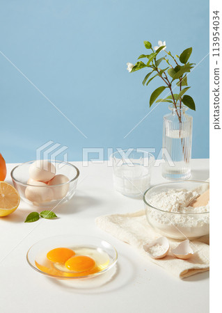 Preparation for breakfast or brunch with many ingredients, flour, egg, milk and lemon decorated by beautiful flower vase. Blank space for displaying culinary product 113954034