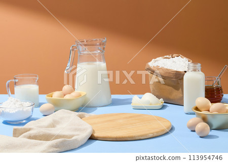 Wooden chopping board with empty space decorated with flour bag, eggs, honey and milk. Concept of cooking. Blank space on the cutting board to show your product Wooden chopping board with empty space decorated with flour bag, eggs, honey and milk. Concept of cooking. Blank space on the cutting board to show your product 113954746