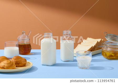 Empty label bottles filled with milk displayed with dishes of bread and sandwiches. A jar of honey, a milk cup and and a jar of jam are arranged on brown background Empty label bottles filled with milk displayed with dishes of bread and sandwiches. A jar of honey, a milk cup and and a jar of jam are arranged on brown background 113954761