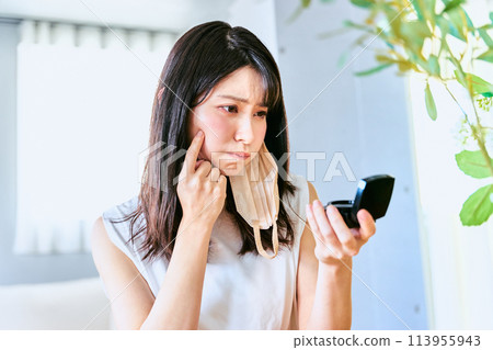 A woman in her 30s with sensitive skin is dissatisfied with her facial skin condition and is worried about it while looking at the mirror and getting ready to go to work at home. A woman in her 30s with sensitive skin is dissatisfied with her facial skin condition and is worried about it while looking at the mirror and getting ready to go to work at home. 113955943