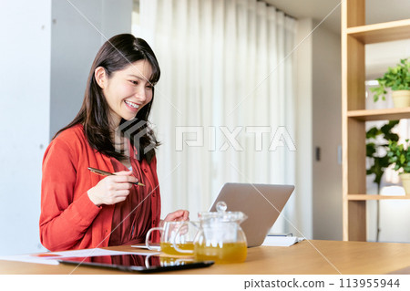 A female student in her 20s or 30s taking online classes at school on a laptop in her living room 113955944