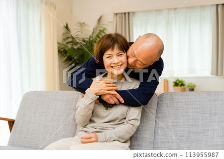 客廳沙發上，丈夫從背後擁抱親吻妻子，這是一對中年夫妻的恩愛表情。 113955987