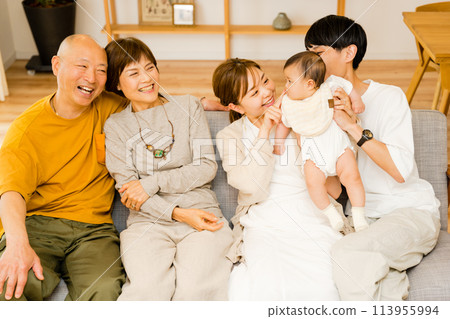 A large family of five people from three households: senior grandparents, a newborn baby, and parents, spending time together in the living room at home A large family of five people from three households: senior grandparents, a newborn baby, and parents, spending time together in the living room at home 113955994