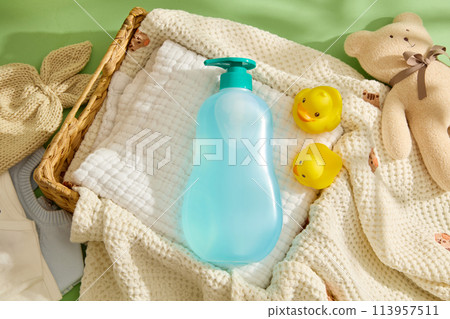 Template for baby products advertising, green background against knitted towel, a rattan basket contains a linen towel below a blue bottle without label. Top view, mockup for design Template for baby products advertising, green background against knitted towel, a rattan basket contains a linen towel below a blue bottle without label. Top view, mockup for design 113957511