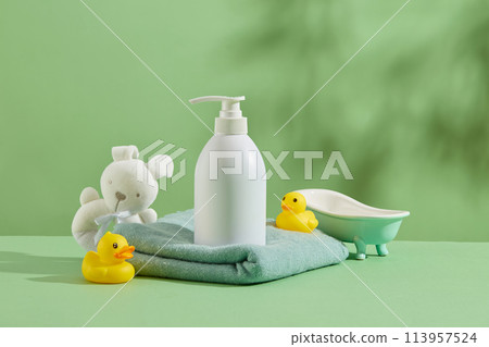 Sea green color background against on some baby bath accessories, a unlabeled white bottle placed on blue bath towel, surrounded by baby toys and bathtub. Copy space for text with front view Sea green color background against on some baby bath accessories, a unlabeled white bottle placed on blue bath towel, surrounded by baby toys and bathtub. Copy space for text with front view 113957524