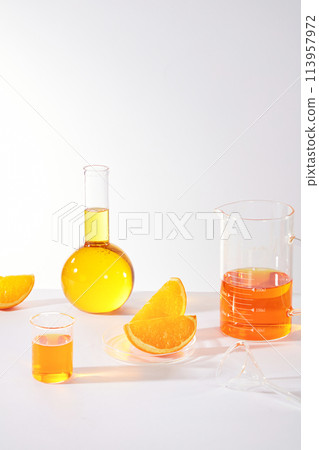 Minimal background with laboratory and orange concept, boiling and beaker filled in orange fluid extract from orange decorated by some orange pieces. Advertising photo for cosmetic, beverage or vegeta Minimal background with laboratory and orange concept, boiling and beaker filled in orange fluid extract from orange decorated by some orange pieces. Advertising photo for cosmetic, beverage or vegeta 113957972