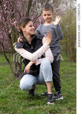 Mom and son high five with their hands in a cherry blossom garden 113960526