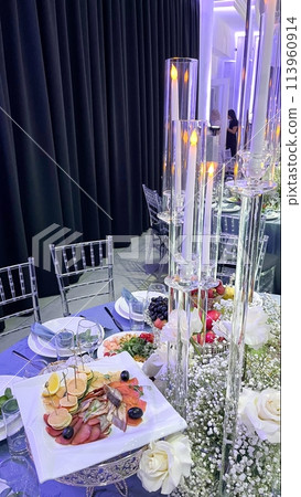 A beautifully set table with elegant floral arrangements and glowing candles, creating a luxurious and sophisticated dining ambiance. 113960914