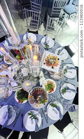 A beautifully set table featuring an elegant floral centerpiece, flickering candles, and an assortment of stylish dinnerware. 113960916