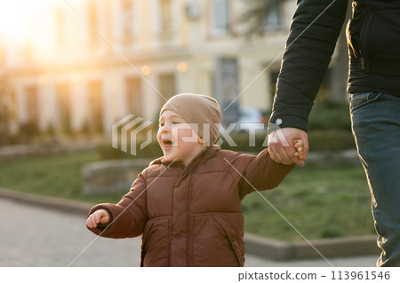 A happy three year old son walks hand in hand with his dad in the city on a sunny spring day. Family fun time and leisure. Spending time. Close up A happy three year old son walks hand in hand with his dad in the city on a sunny spring day. Family fun time and leisure. Spending time. Close up 113961546