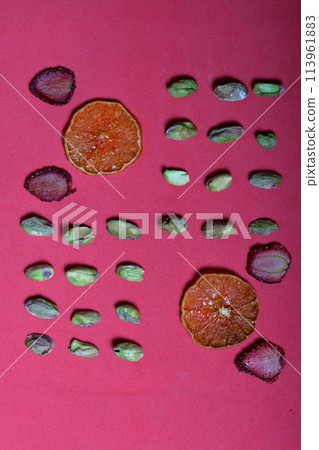 Pistachios are laid out on the table to decorate desserts. Near a few slices of dried mandarin and strawberry. 113961883