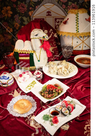 Kazakh dastarkhan featuring beshbarmak, manty, samsa, baursak, yurt-shaped tent, camel saddle, and more traditional dishes. 113961916