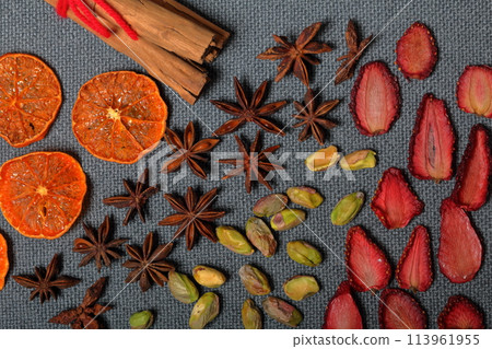Dried tangerines and strawberries, cut into pieces to decorate the dessert. Nearby are pistachios, anise and cinnamon sticks tied with red thread. On a gray background. Dried tangerines and strawberries, cut into pieces to decorate the dessert. Nearby are pistachios, anise and cinnamon sticks tied with red thread. On a gray background. 113961955