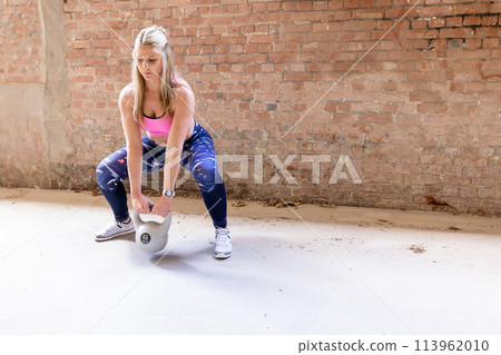 Focused Athlete Performing Kettlebell Squats in a Minimalistic Gym Setting 113962010