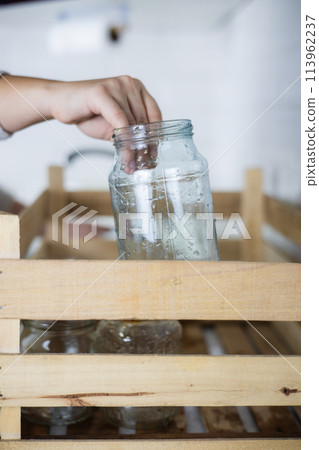 Vertical. A housewife reaches out and places an old glass jar in a recycling bin. A housewife collects unwanted glass jars and bottles at home to send for recycling. Glass recycling concept. 113962237