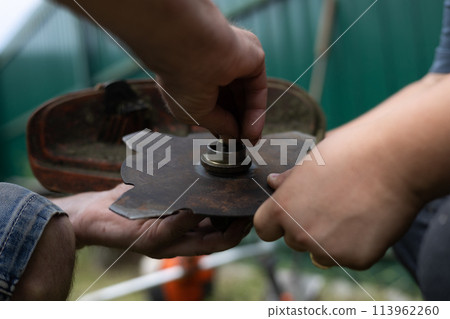 Close-up of tightening the nut on the metal disc on a grass trimmer. In order to mow tall, dense grass, put a sharp metal disc on the trimmer. Concept of preparing a dimmer for grass. Close-up of tightening the nut on the metal disc on a grass trimmer. In order to mow tall, dense grass, put a sharp metal disc on the trimmer. Concept of preparing a dimmer for grass. 113962260