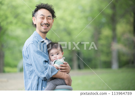 Dad holding a baby outdoors in fresh greenery 113964789