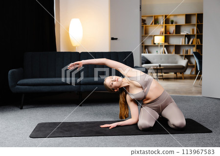 Young sporty woman practicing yoga, doing Revolved Head to Knee Forward exercise, wearing sportswear, sitting on the floor in living room Young sporty woman practicing yoga, doing Revolved Head to Knee Forward exercise, wearing sportswear, sitting on the floor in living room 113967583