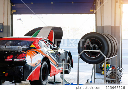Back view Nascar Whelen euro series racing sportscar vehicle Motorsport Arena garage box race track pit paddock hanged on hydraulic jack lift with open hood. European motor auto sport competition Back view Nascar Whelen euro series racing sportscar vehicle Motorsport Arena garage box race track pit paddock hanged on hydraulic jack lift with open hood. European motor auto sport competition 113968526