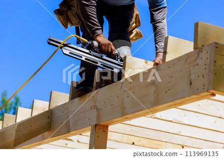 Framer worker installing beams using air nails hammer in nailing wooden frame 113969135
