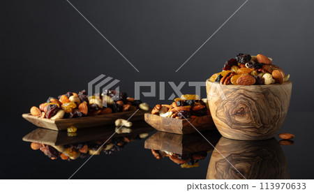 Mix of various nuts and raisins on a black reflective background. 113970633