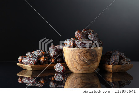Dates in wooden dish on a black background. 113970641