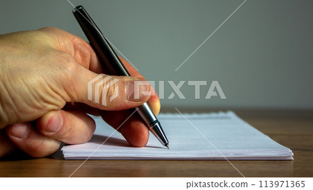 Notebook and fingers of a working man with a pen on wood table. 113971365