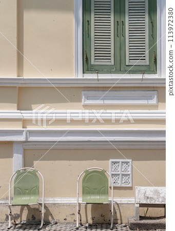 Two vintage sebel stacking steel chairs and Double green wooden shutters windows on yellow wall. Two vintage sebel stacking steel chairs and Double green wooden shutters windows on yellow wall. 113972380